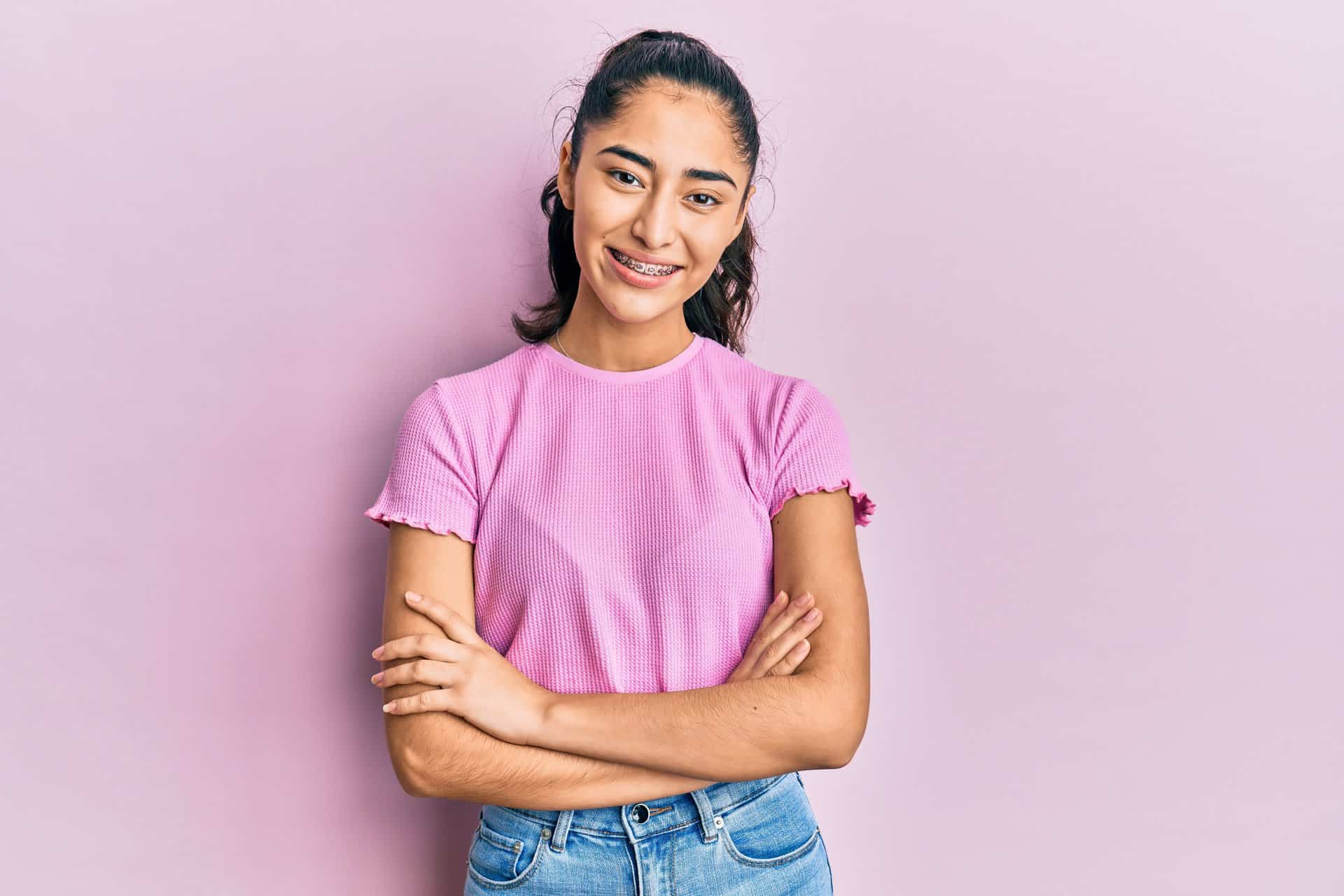 Hispanic teenager girl with dental braces wearing casual clothes happy face smiling with crossed arms looking at the camera. positive person.