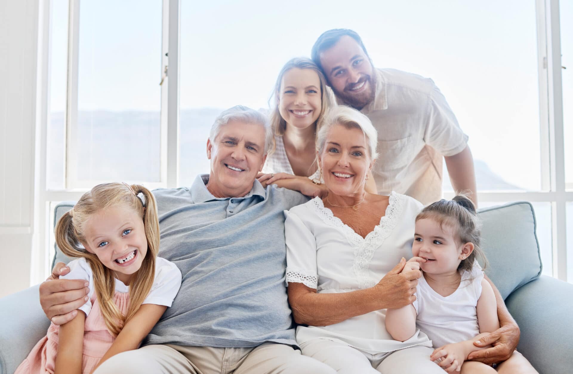 Family, love and children with a girl, parents and grandparents sitting on a living room sofa at home together. Kids, happy or bonding with a senior man, woman and relatives on a couch during a visit